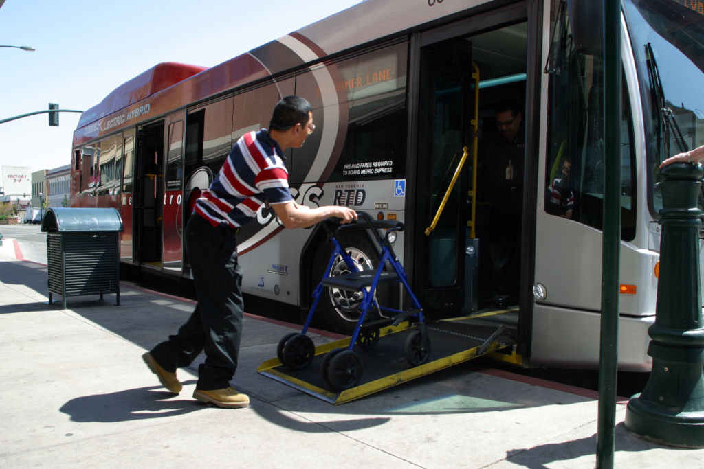 Man using a walker ascends a ramp to board a bus