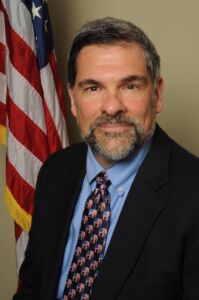 photo of Michael Restuccia. He is wearing a black jacket, blue dress shirt, and a tie with a patriotic elephant pattern.