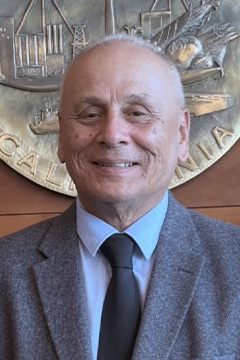 Board Member Donald Tafoya wearing a gray jacket, light shirt, and dark tie, smiling with the San Joaquin County seal displayed in the background.